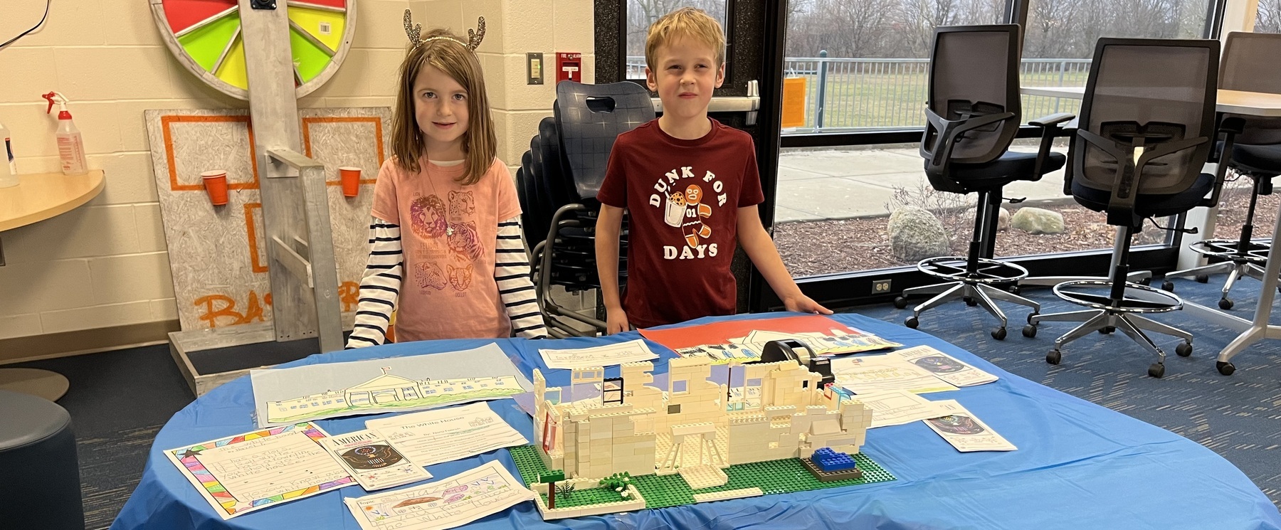 A male and female 1st grade student pose in front of a model of the White House made out of Lego.