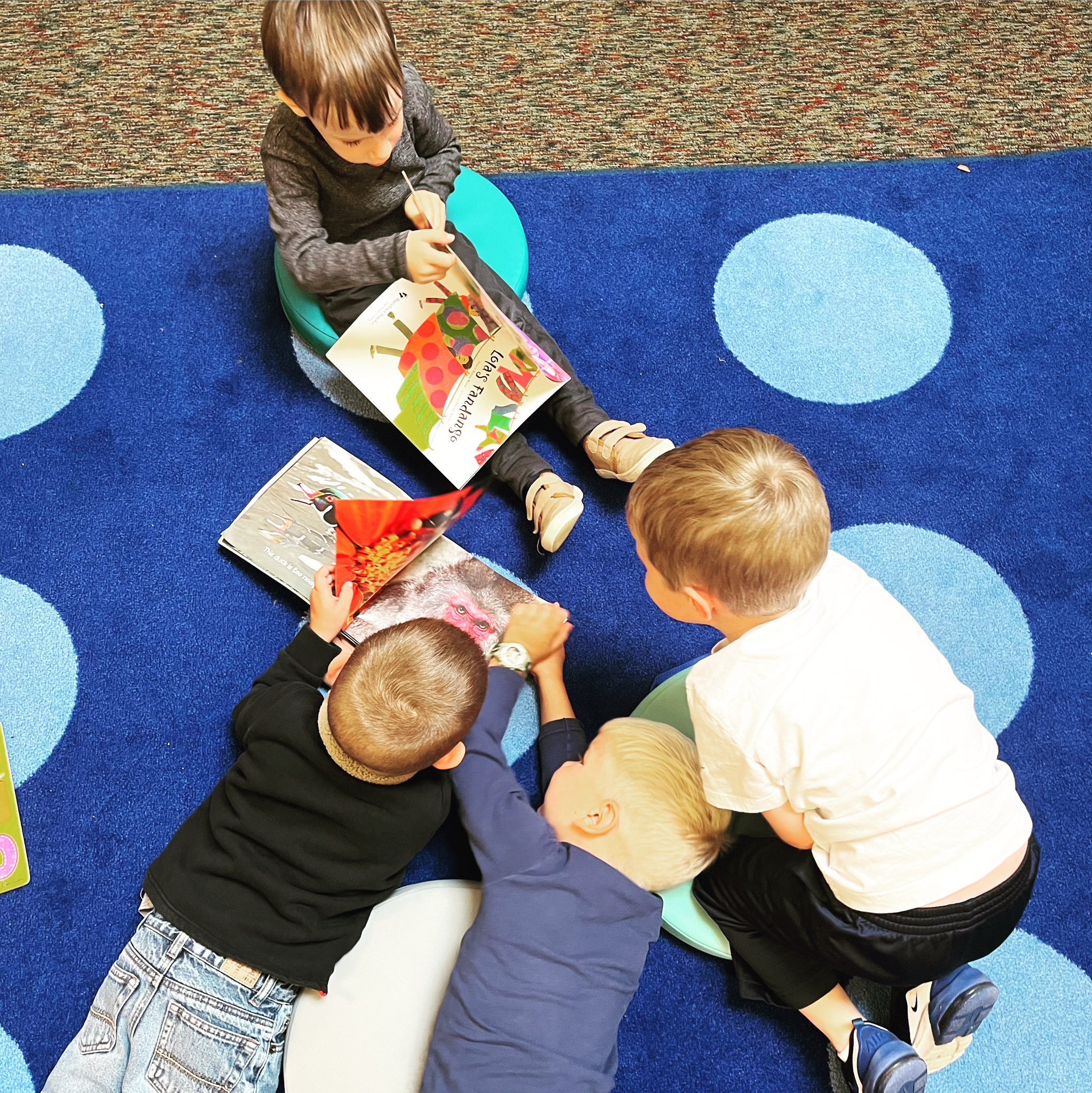 Decorative image of 4 preschool boys reading a book together.